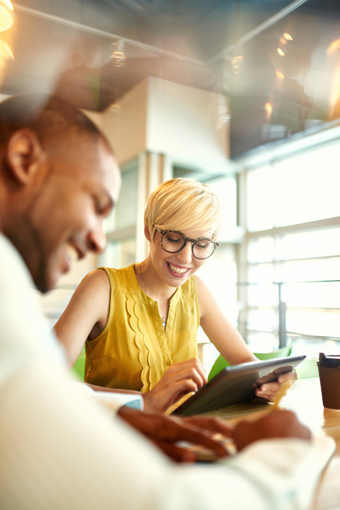 Two creative millenial small business owners working on social media strategy using a digital tablet while sitting at desk